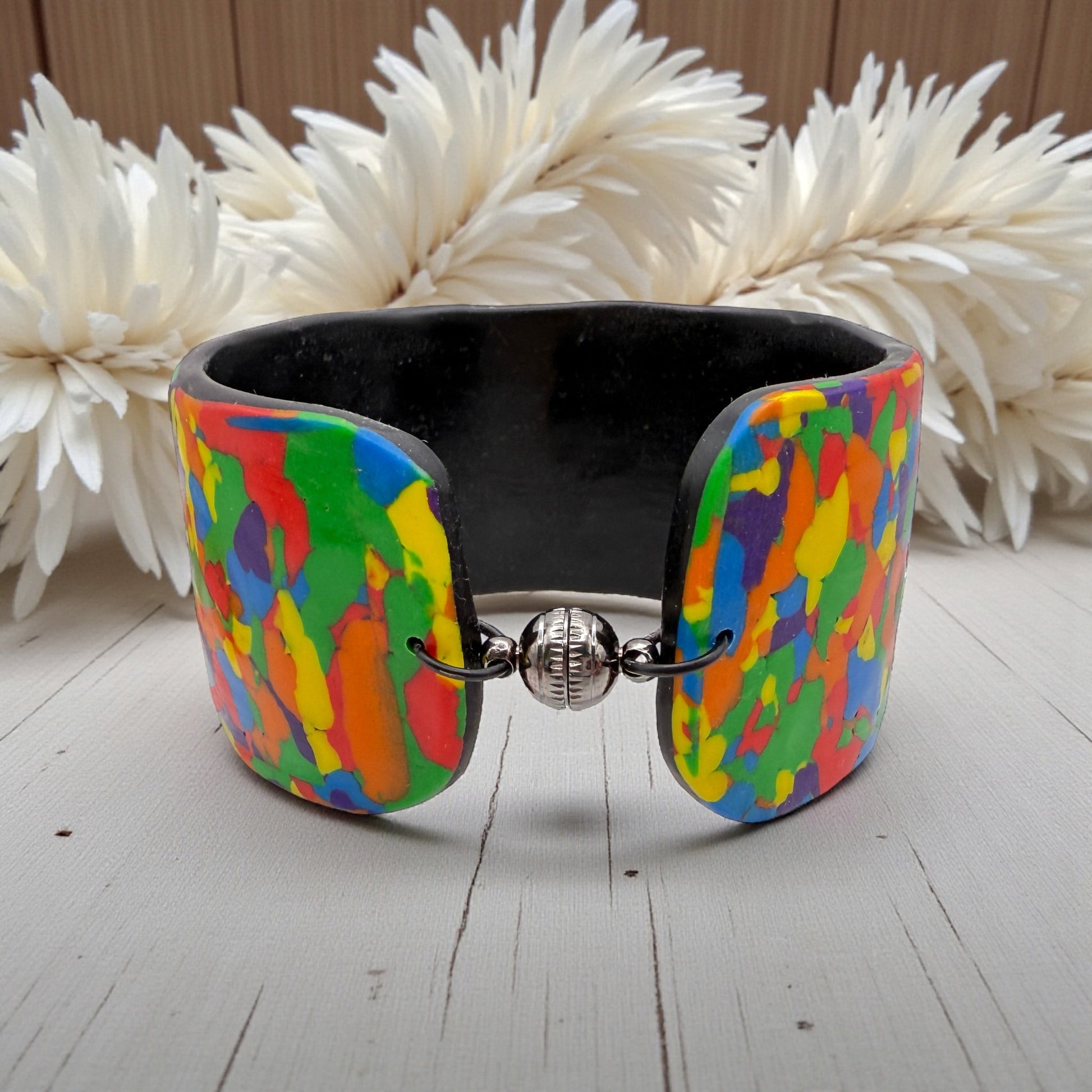 These Pretty Things Pixel Party Cuff on a neutral table with a beige feather boa in the background