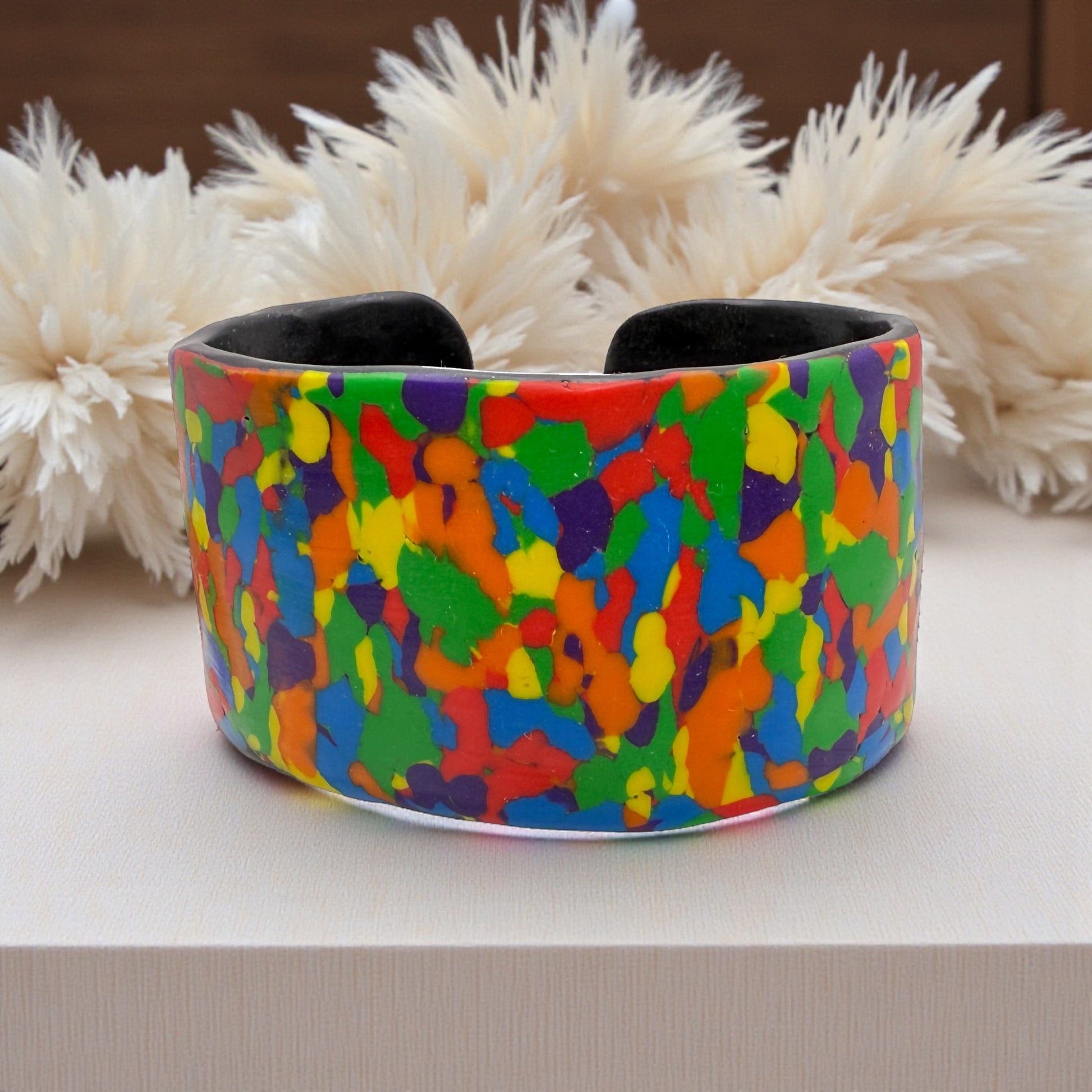 These Pretty Things Pixel Party Cuff on a neutral table with a beige feather boa in the background
