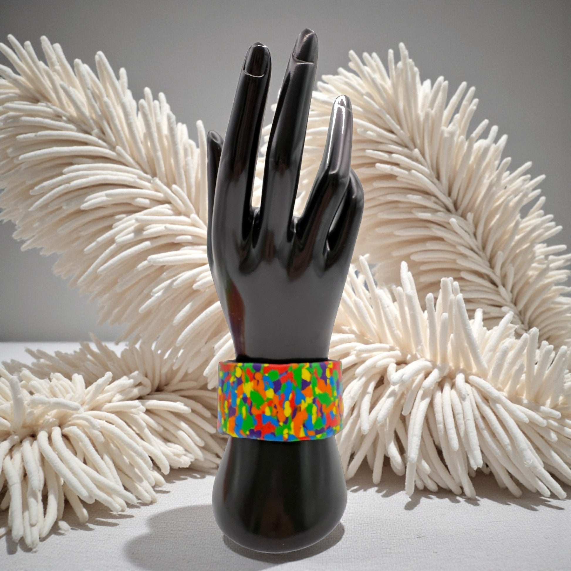 These Pretty Things Pixel Party Cuff on a black hand mannequin with a beige feather boa in the background