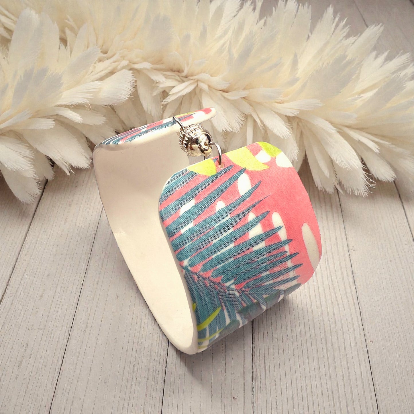 These Pretty Things Rainbow Forest Cuff on a table with a creamy white feather boa in the background