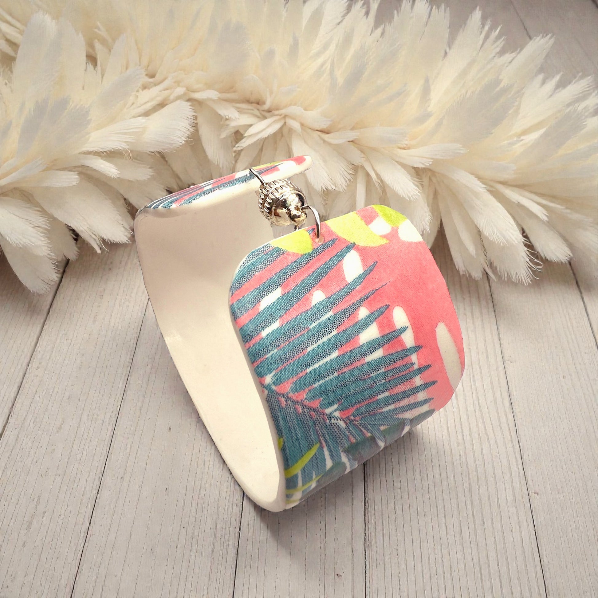 These Pretty Things Rainbow Forest Cuff on a table with a creamy white feather boa in the background