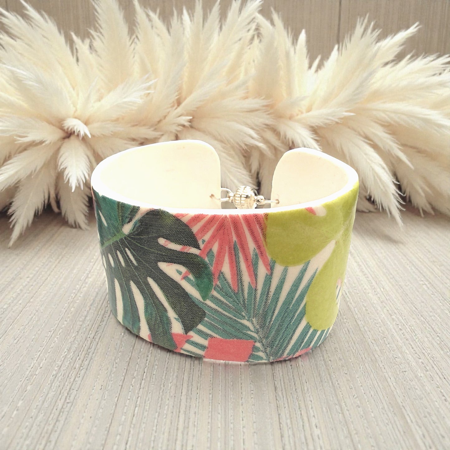 These Pretty Things Rainbow Forest Cuff on a table with a creamy white feather boa in the background