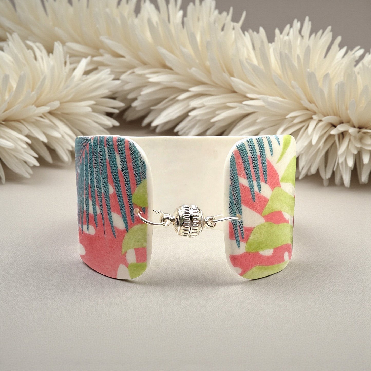 These Pretty Things Rainbow Forest Cuff on a table with a creamy white feather boa in the background