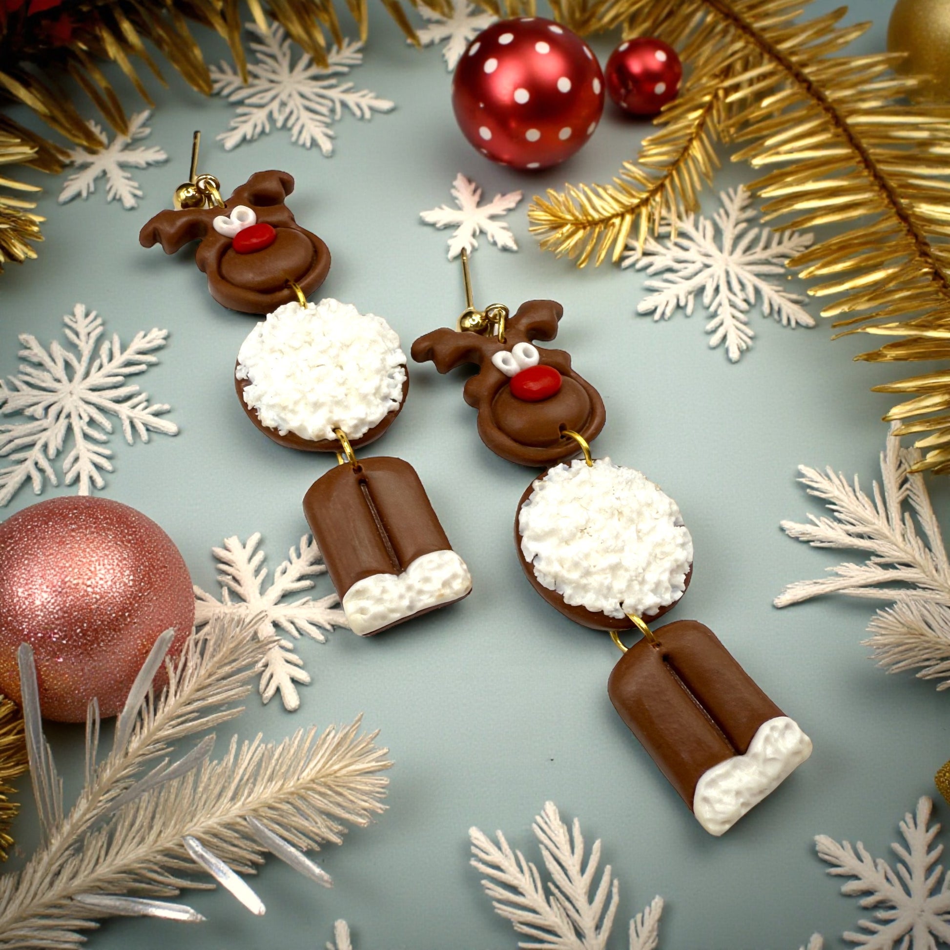 Dark brown reindeer earrings with a white fur-like tummy. on a festive background with gold and red decorations with snowflakes.