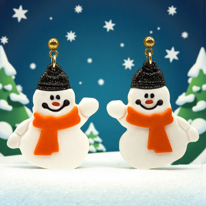 Snowmen earrings with sparkly black hats and orange scarves against a snowy background.