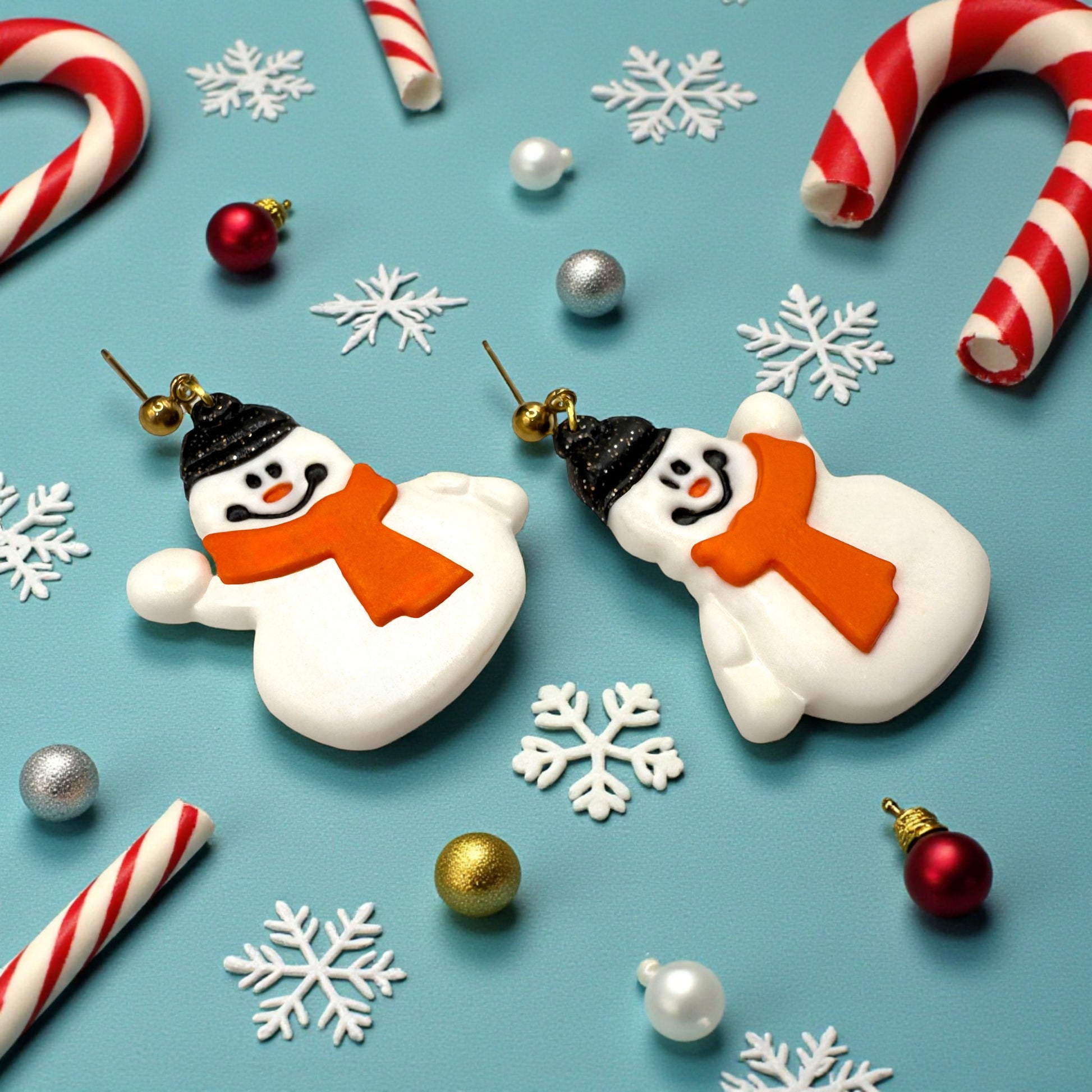 Snowmen earrings with sparkly black hats and orange scarves with candy canes, snowflakes & baubles on a blue background.