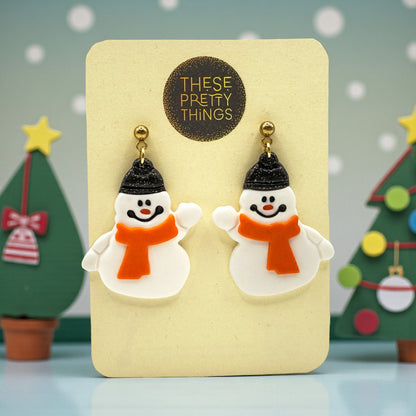Snowmen earrings on a 'These Pretty Things' presentation card with Christmas trees in the background.