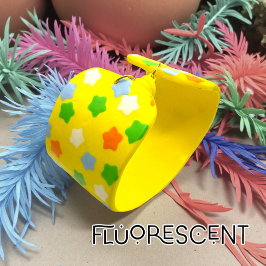 These Pretty Things Yellow Fluorescent Cuff on a neutral base with multiple coloured feather boas in the background