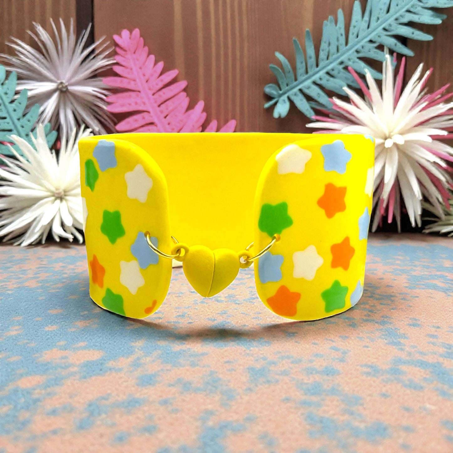 These Pretty Things Yellow Fluorescent Cuff on a neutral base with multiple coloured feather boas in the background