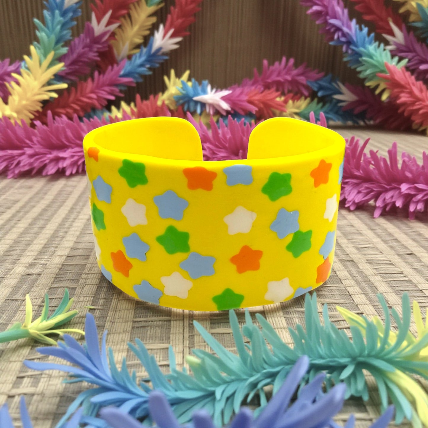 These Pretty Things Yellow Fluorescent Cuff on a neutral base with multiple coloured feather boas in the background