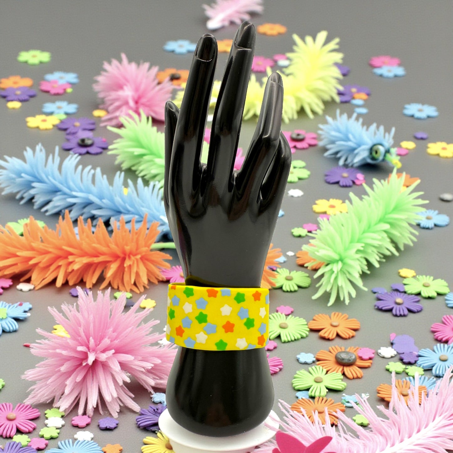 These Pretty Things Yellow Fluorescent Cuff on a black hand mannequin with colourful feather and flower confetti in the background